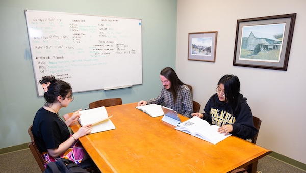 students working a a large table with a whiteboard behind them