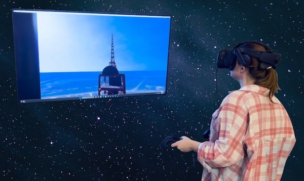 Student wearing VR headset. The simulation she is using is mirrored on a wall-mounted display.