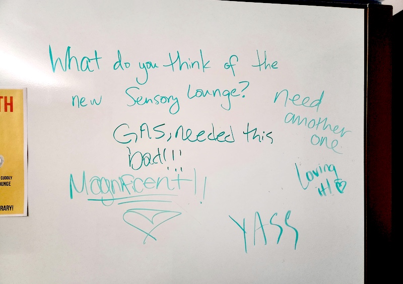 Whiteboard asking students what they think of the Sensory Lounge. Responses say "Magnificent!," "YASS," "need another one," "GAS, needed this bad!!," and "Loving it!"