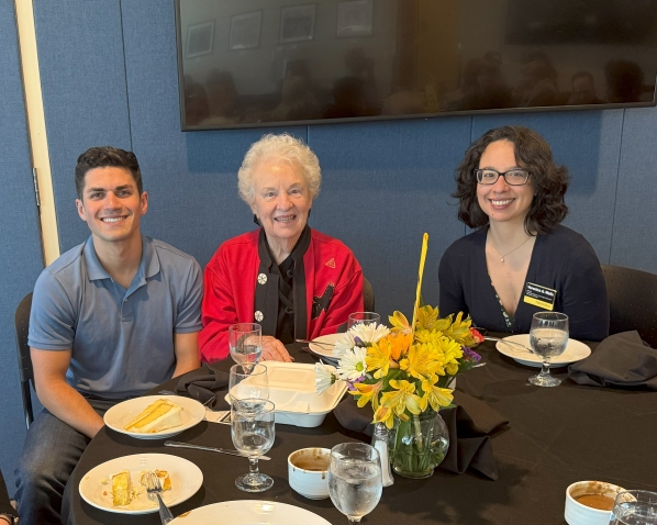 Photograph of male student in blue shirt, scholarship donor woman in red blazer, library personnel woman in black shirt with name tag