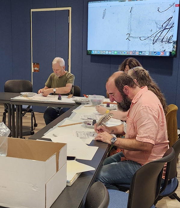 Photo of a man in a red shirt and a woman with grey hair working on a handwritten document