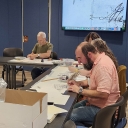 Photo of a man in a red shirt and a woman with grey hair working on a handwritten document