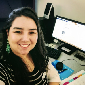 Photograph of Sai Estep at work, dark long hair, dark eyes, black striped shirt