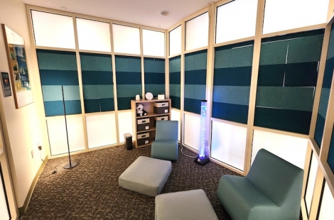 Small room with two floor rockers, a bubble tube, low lighting, and shelves containing small sensory items