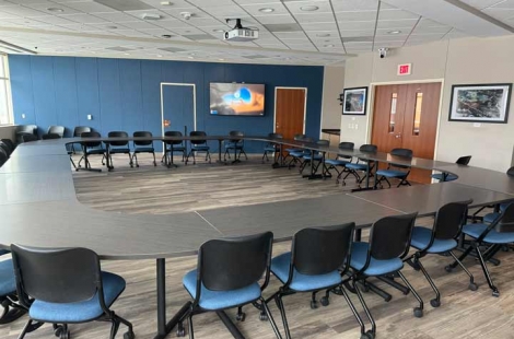 Conference room 421, with tables and chairs arranged in a circle, a projector, and additional wall displays on the sides of the room