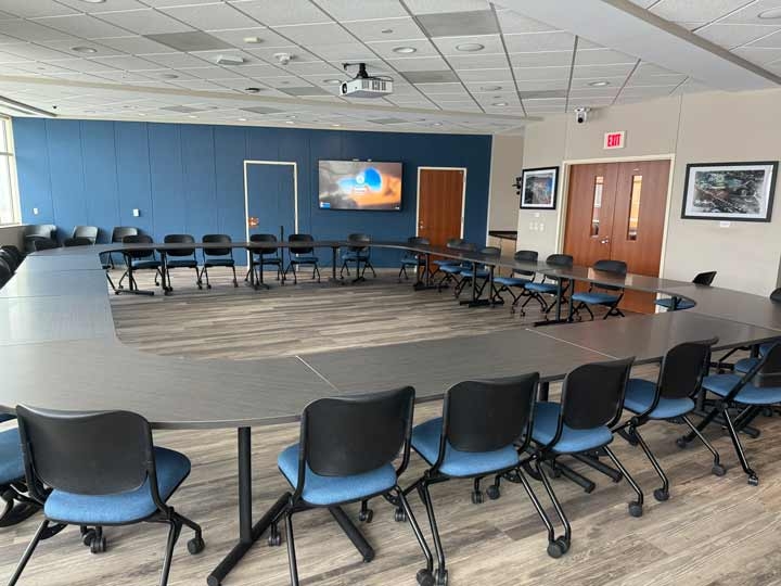 Conference room 421, with tables and chairs arranged in a circle, a projector, and additional wall displays on the sides of the room