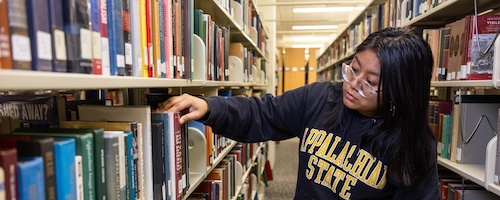 A library student employee wearing an App State sweatshirt locates a book in the stacks