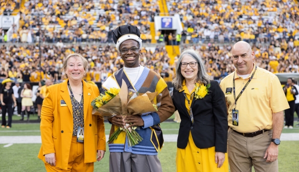 Bright standing on the football field wearing the King of the Rock Crown and smiling, surrounded by the Chancellor, Provost, and Dr. JJ Brown all in App State colors
