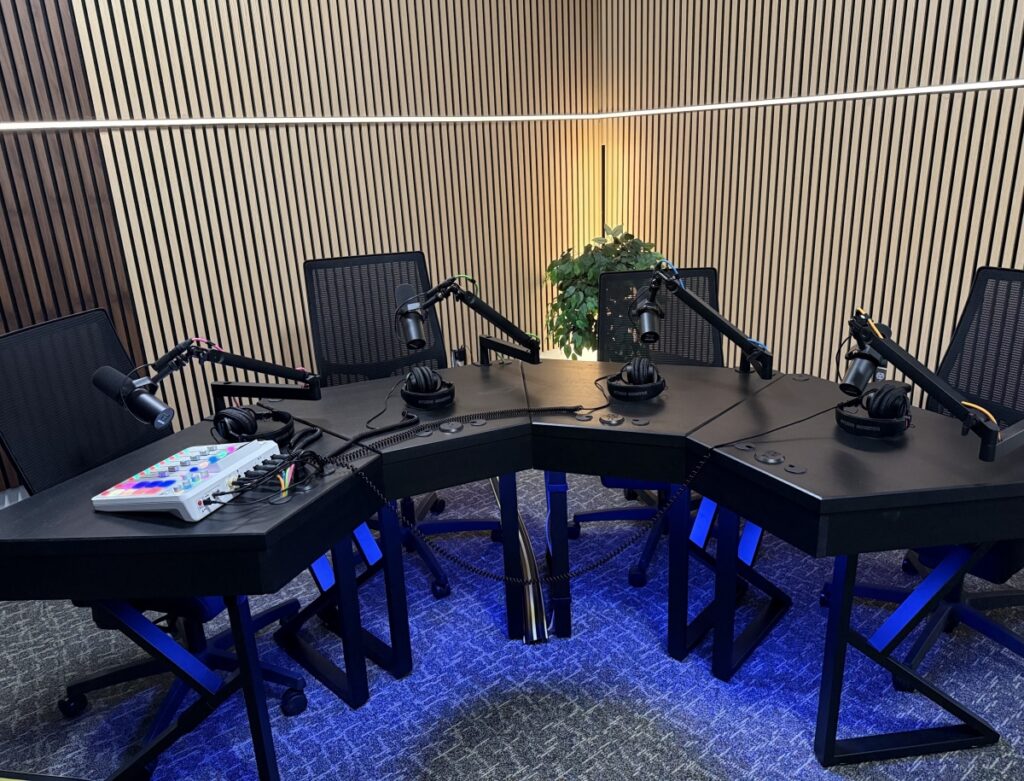 Semi-circular desk with four microphones and a RØDECaster Pro II mixer