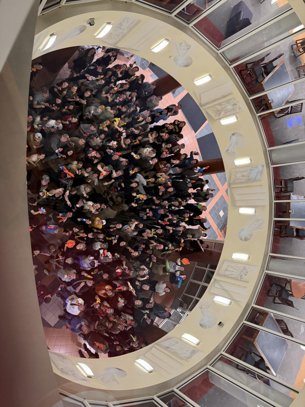 Humans vs. zombies game participants, dressed for the event, aiming nerf blasters at the photographer on the 2nd floor of the building